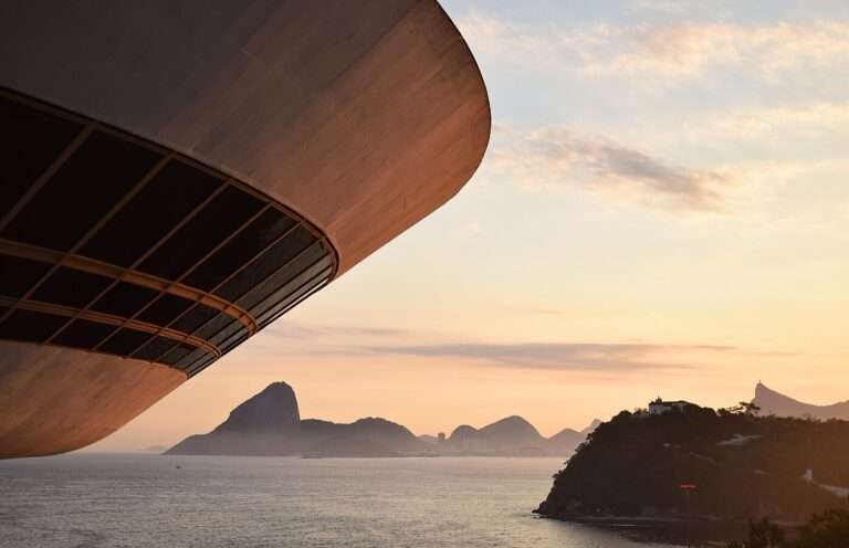 The curved underside of Niterói's Contemporary Art Museum at sunset, with Sugarloaf and Corcovado across the bay