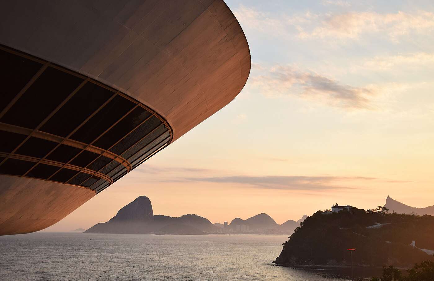 The curved underside of Niterói's Contemporary Art Museum at sunset, with Sugarloaf and Corcovado across the bay